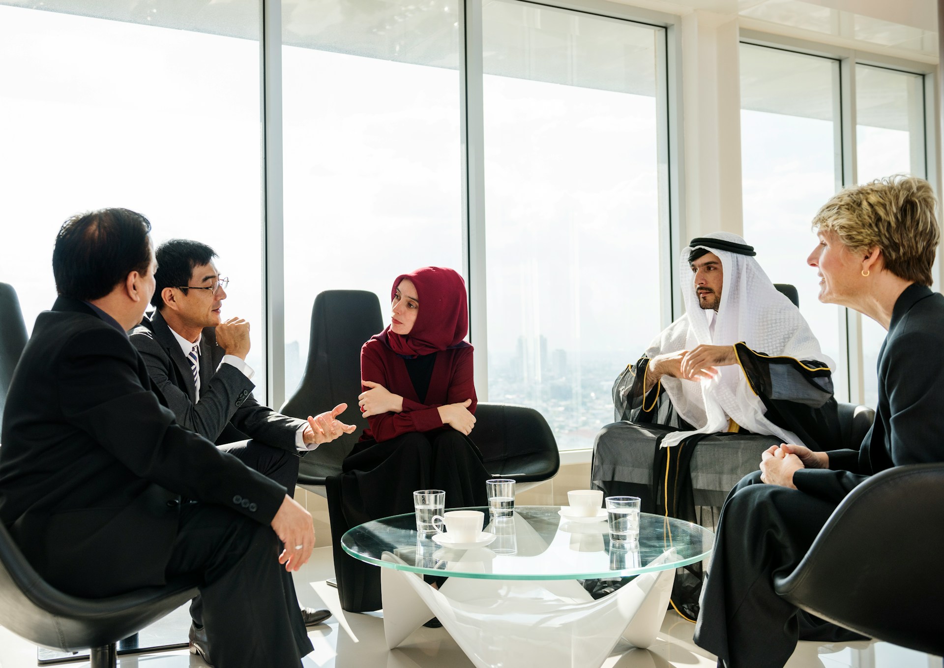A cross-border working meeting — partners from Europe and the Gulf around a table in a high-rise office, mid-conversation.
