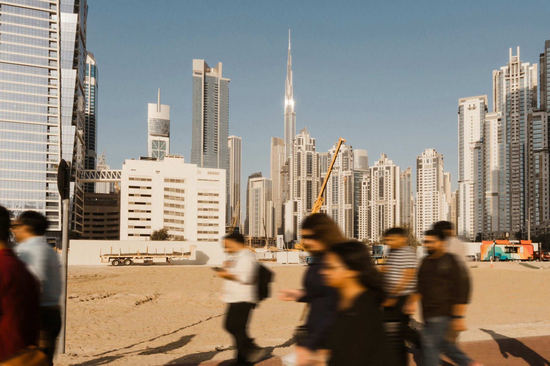 A Gulf-city skyline at golden hour with motion-blurred commuters in the foreground — the everyday market microinsurance reaches.
