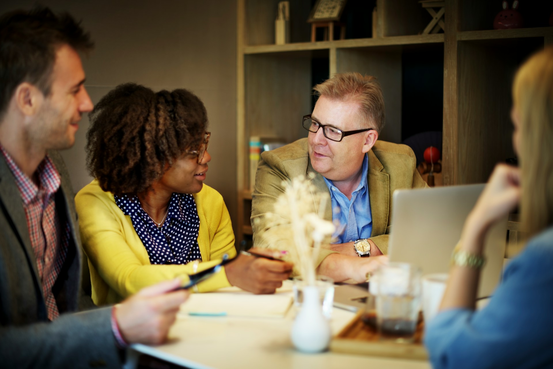 A diverse team of executives in discussion around a laptop at a boardroom table.